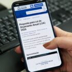 Mulher segura celular e na tela está escrito "proposta para lei de orçamento anual"
