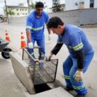 Dois homens instalam cesto de metal em boca de lobo
