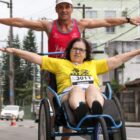 Mulher em cadeira de rodas participa de corrida sendo conduzida por homem