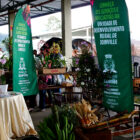 Imagem mostra galpão onde ocorre a Feira Direto do Campo, com cadeiras, mesa, flores à venda e publicidade sobre os serviços da Unidade de Desenvolvimento Rural de Joinville