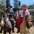 Dois homens vestidos com roupas típicas do RS estão montados em cavalos