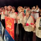 Idosos em palco seguram faixa com nome de grupo, flores e sorriem