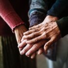 Quatro mãos de pessoas idosas juntas, uma sobre a outra