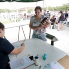 Mulher em pé segura cão no colo enquanto mulher sentada preenche ficha