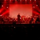 Músicos em palco tocando diferentes instrumentos sob iluminação vermelha