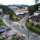 Imagem aérea das rua Arthur Baechtold na esquina com XV de Novembro, com sinalização, carros trafegando. Há casas e prédios ao redor