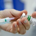 Mão segurando agulha e outra mão frasco de vacina