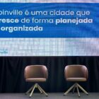 Vice prefeita, mulher com cabelos curtos e loiros, segura microfone e fala na frente de um telão