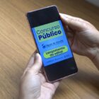 Pessoa segura celular na mão e na tela tem informações sobre lançamento de edital de concurso público da Águas de Joinville
