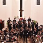 Músicos vestidos de preto, alguns em pé e outros sentados, tocam instrumentos