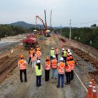 Imagem aérea de grupo de pessoas com coletes refletivos e capacetes próximas à futura Ponte Joinville