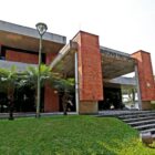 Prédio com estrutura em concreto e tijolos à vista com gramado e escada de acesso na frente