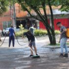 Homens trabalham em limpeza de praça com lava jato e vassouras