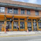 Homens em pé pintam fachada de prédio laranja com detalhes em verde