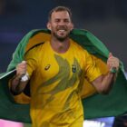 Homem branco de camisa amarela segura bandeira do Brasil com as duas mãos ao redor das costas