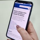 Mão segura celular que mostra a frase Realizar cadastro como escritor de projetos e captador de recursos