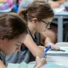 Duas meninas leem e escrevem em caderno, sentadas em sala de aula
