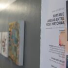 Imagem mostra cartaz da Exposição de arte têxtil “Portas e janelas: entre fios e histórias” em parede com quadros