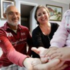 Homem e mulher lado a lado dão as mãos à criança vestida de rosa, cujo rosto não é identificado