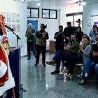 Papai Noel está em pé à frente de diversas pessoas sentadas que aplaudem