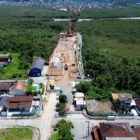 Imagem aérea mostra casas, ruas, área de vegetação, rio e canteiro de obras onde está sendo construída a Ponte Joinville