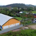 Imagem aérea mostra quadra esportiva próxima à escola, em meio à área de mata