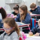 Diversas crianças sentadas com canetas na mão escrevendo em cadernos em sala de aula