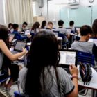Alunos uniformizados em sala de aula usam computadores