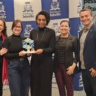 Quatro mulheres e um homem posam para foto, uma delas segura um troféu