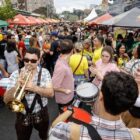 Pessoas reunidas em rua de Joinville com roupas coloridas e instrumentos musicais