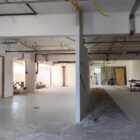 Amplo espaço com pintura branca, tubulação exposta e material de obra