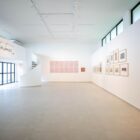 Galeria ampla e iluminada tem paredes pintadas de branco e quadros na parede