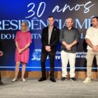 Um homem idoso recebe placa e é observado por outras pessoas