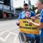Dois agentes do Detrans instalam totem com mensagem de conscientização em placa de trânsito