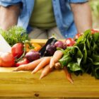 Homem segura caixote de madeira com cenouras, tomates e outros vegetais