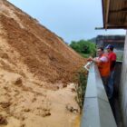 Dois homens olham para amontoado de terra molhada próximo a muro