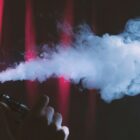Pessoa com rosto de perfil segura cigarro eletrônico na mão e solta fumaça pela boca