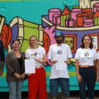 Homens e mulheres em pé em frente a um contêiner colorido em verde com grafite