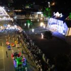 Imagem aérea mostra desfile de Natal com carro alegórico e pessoas na rua