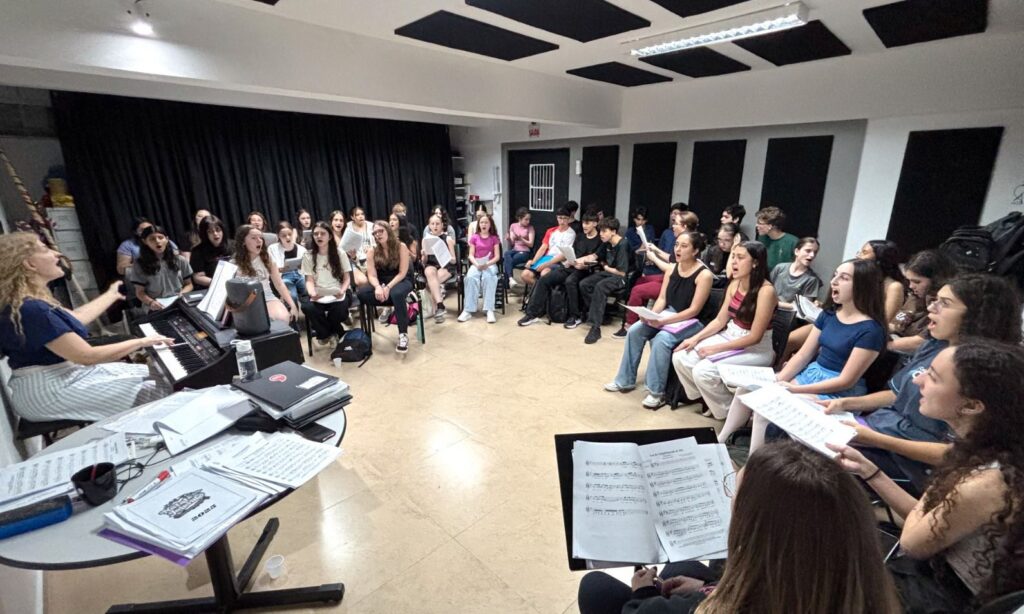 Dezenas de pessoas cantam sentadas em cadeiras em círculo