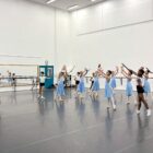 Dezenas de bailarinos e bailarinas ensaiam em sala ampla