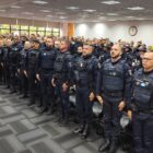 Dezenas de guardas municipais enfileirados usando uniforme em posição de sentido em uma sala ampla