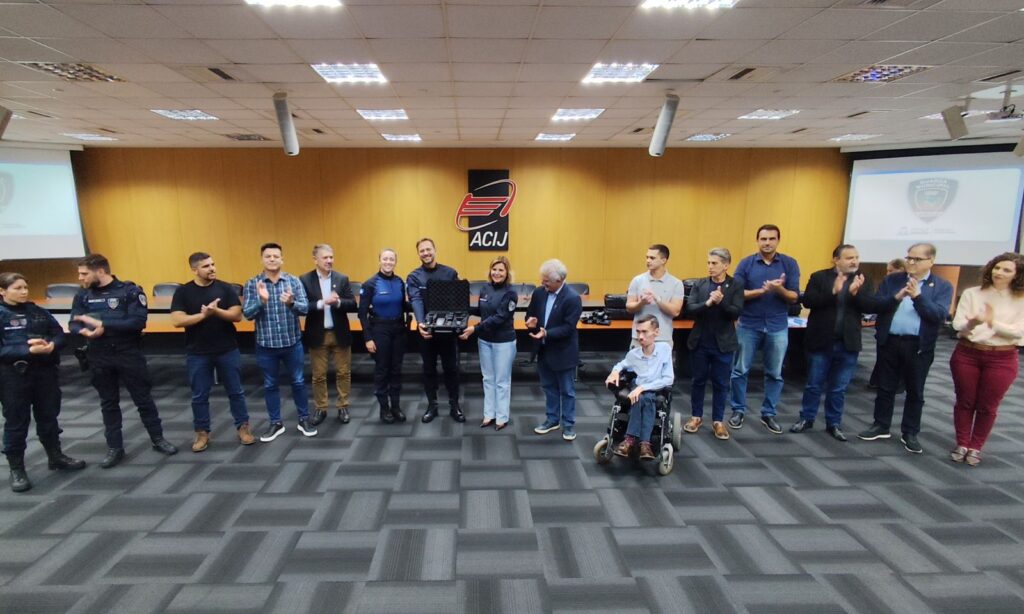 Homens e mulheres posam para foto. Um homem e uma mulher seguram maleta com com equipamento