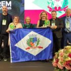 Quatro mulheres e quatro homens posam para foto em palco segurando bandeira de Joinville