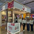 Quatro mulheres e dois homens em pé se posicionam em frente ao estande de Joinville, com sapatilhas e flores, entre outros elementos