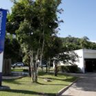 Prédio branco, com gramado e árvores ao redor, com placa vertical escrito museu de sambaqui