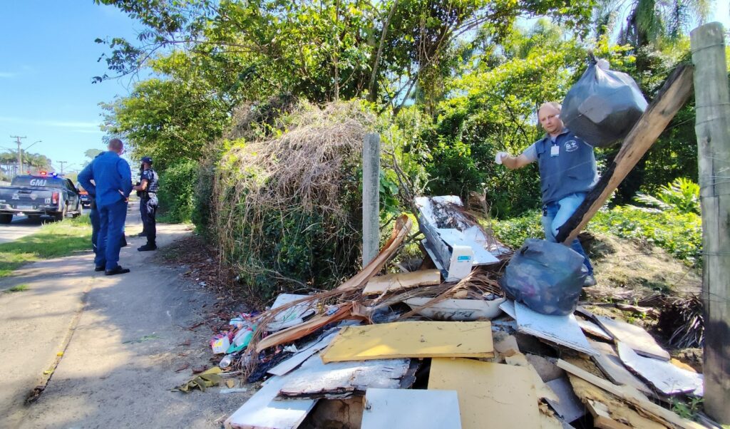 Homem com luvas e colete recolhe lixo em área de mato