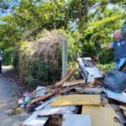 Homem com luvas e colete recolhe lixo em área de mato