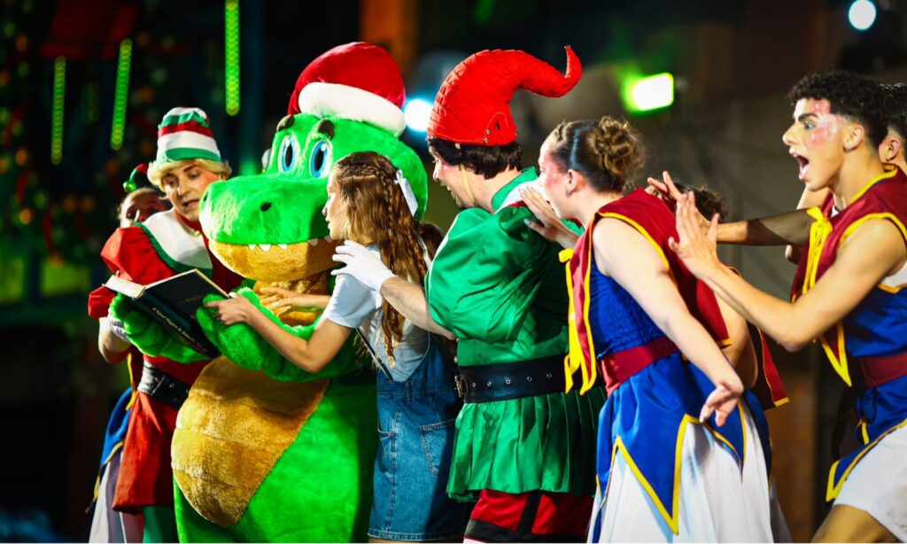 Cena do espetáculo de Natal mostra jacaré Fritz e outros personagens em pé, contracenando no palco