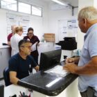 Homem em pé conversa com outro homem atrás de balcão em unidade de saúde